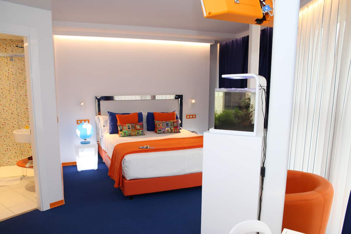 Una habitación de hotel moderna con una cama grande, un escritorio pequeño, un globo terráqueo y una ventana con cortinas.