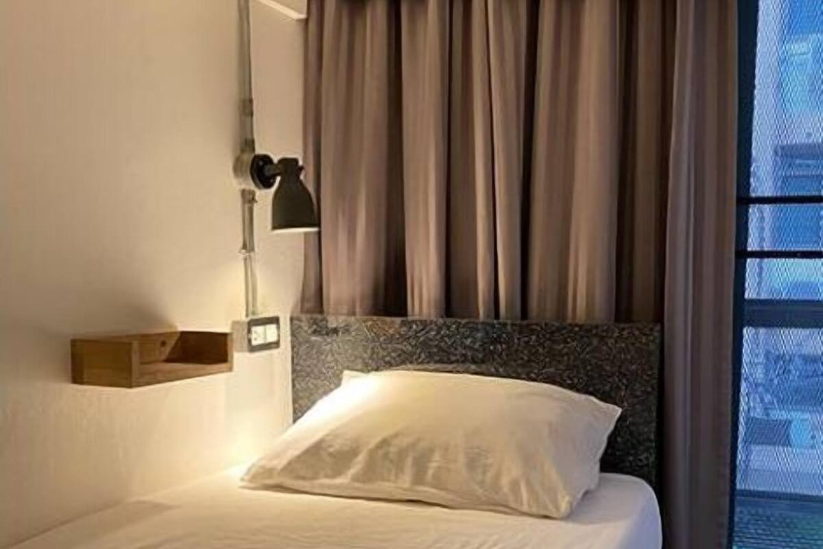 Hotellihuone, jossa on sänky, yöpöytä, lamppu ja ikkuna, jossa on verhot.