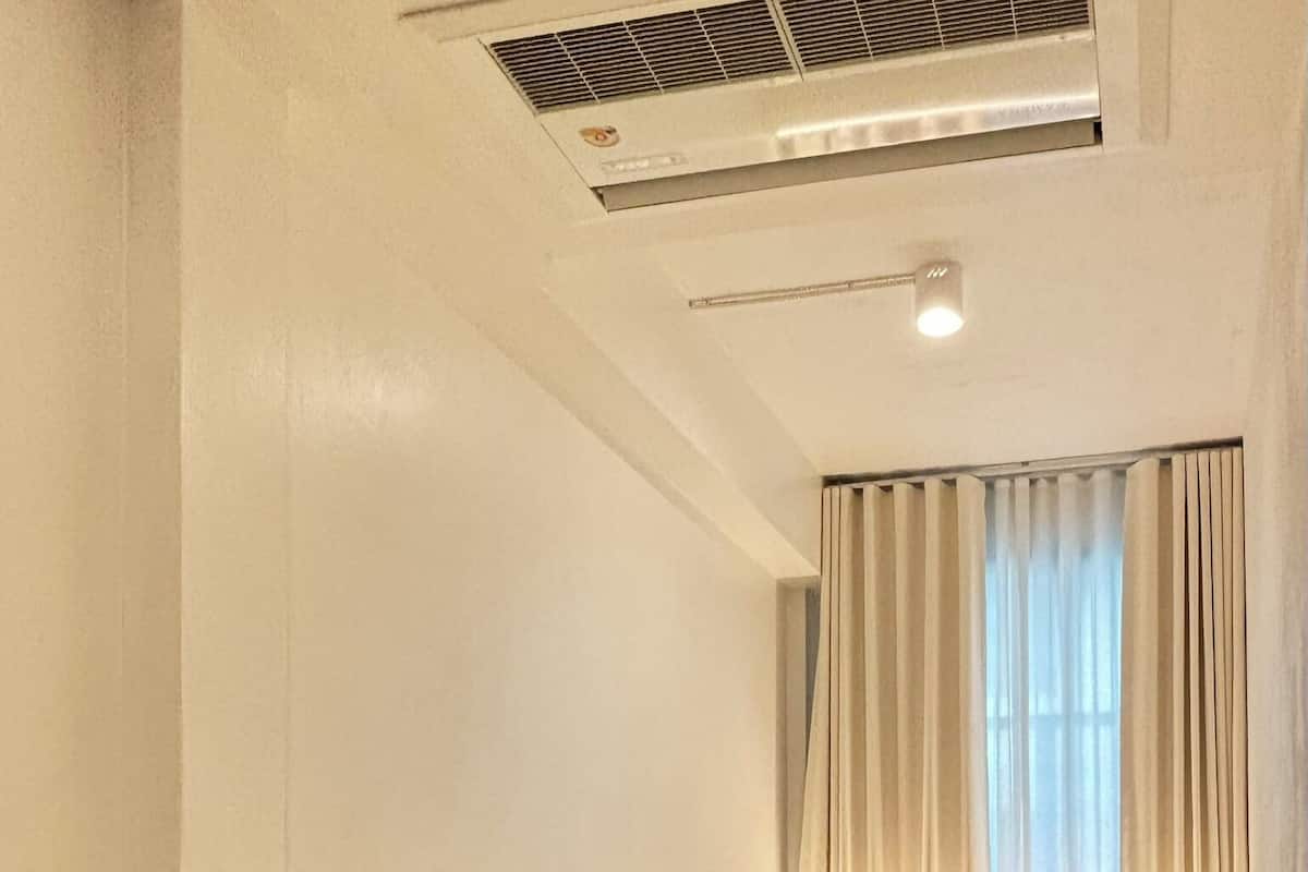 Hotellihuone, jossa on kaksi sänkyä, ilmanvaihtoaukko katossa ja ikkuna, jossa on verhot.