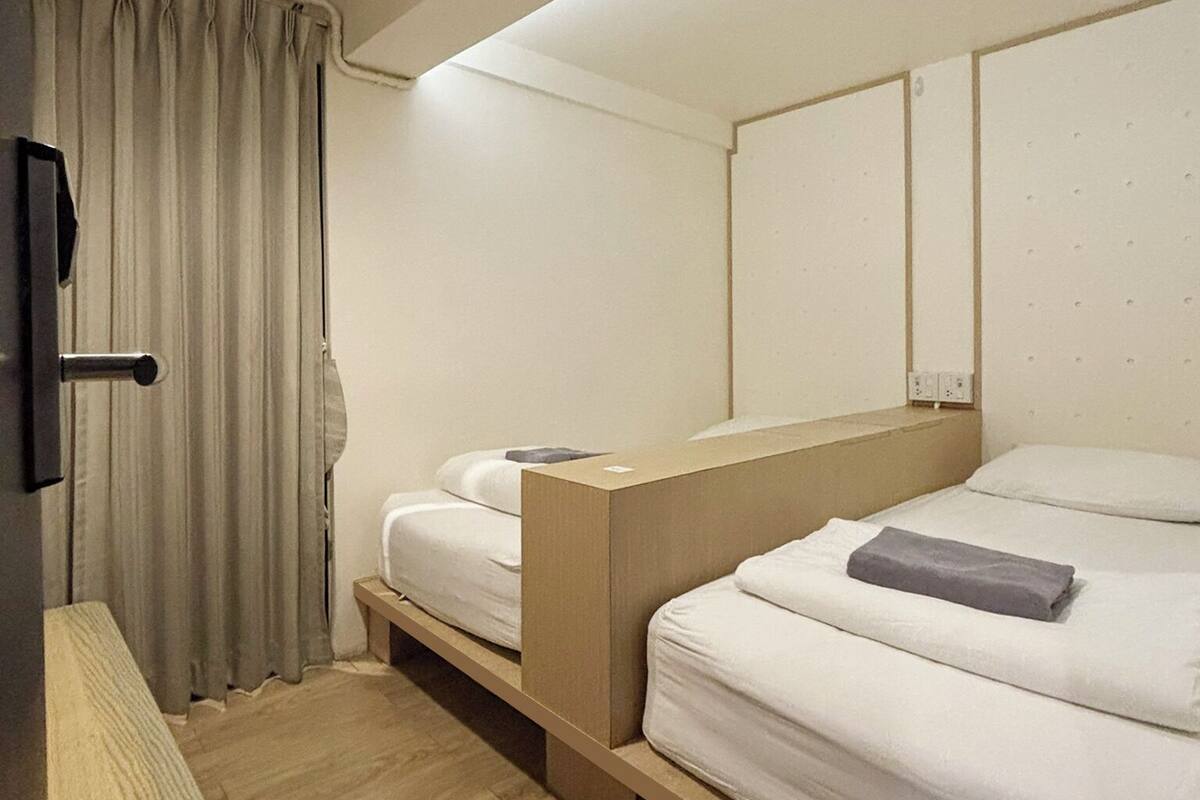 Hotellihuone, jossa on kaksi sänkyä, yöpöytä, lamppu ja kattovalaisin.