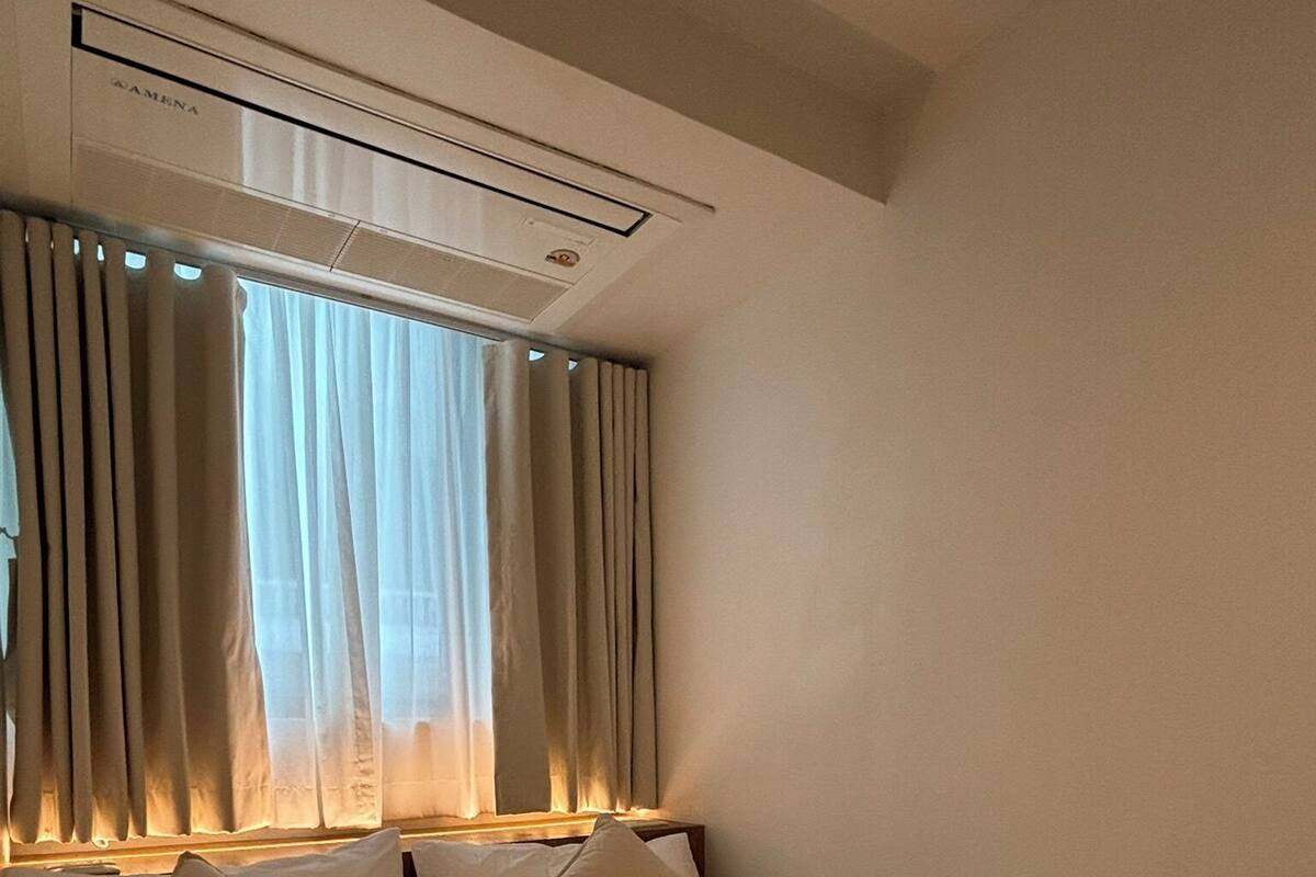 Hotellihuone, jossa on sänky, verhot ja ilmastointilaite.