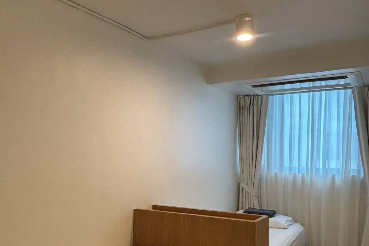 Pieni huone, jossa on yksi sänky, puinen pääty ja ikkuna, jossa on verhot, sekä kattovalaisin.