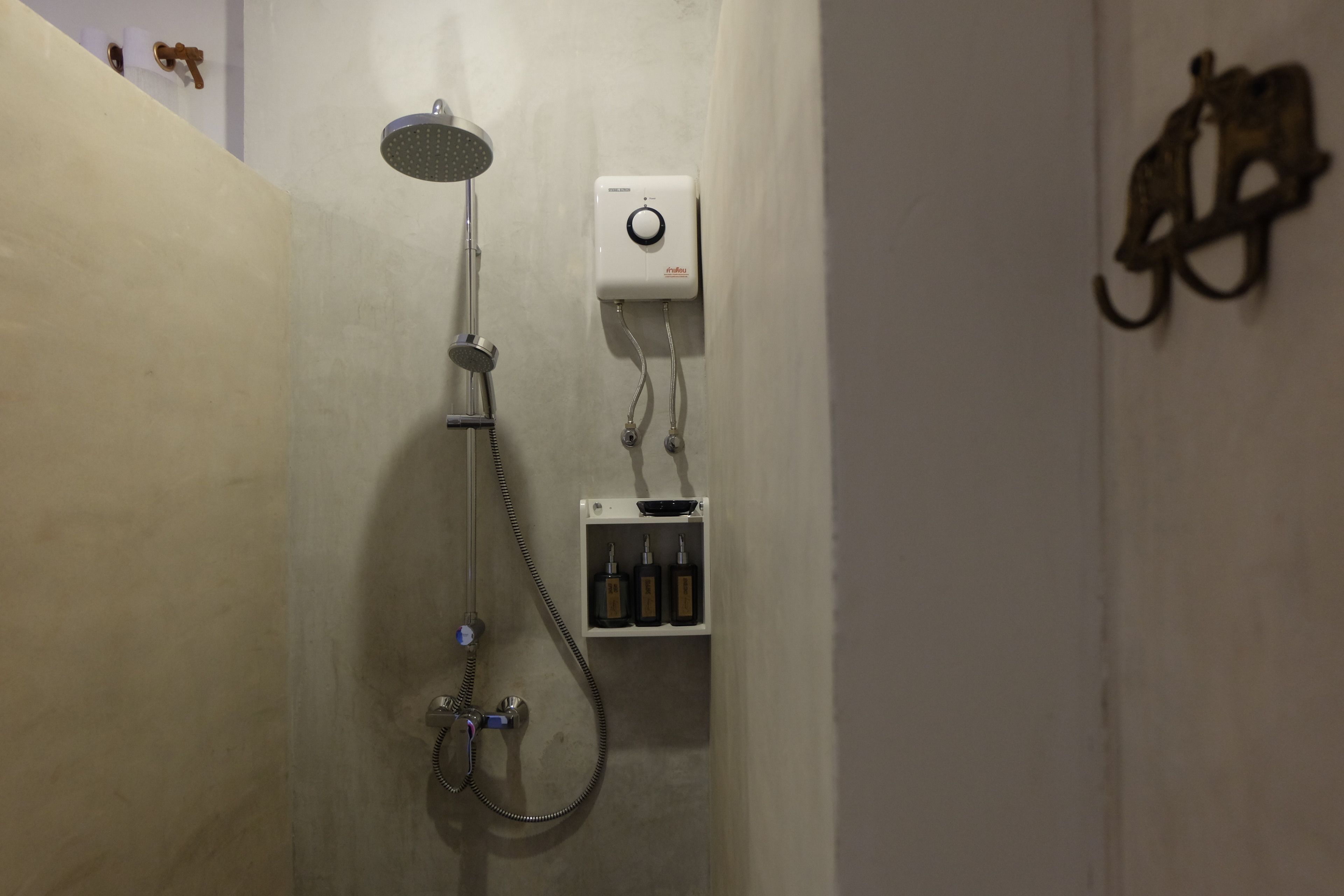 A shower with a handheld showerhead, a wall-mounted control panel, and a soap dispenser.