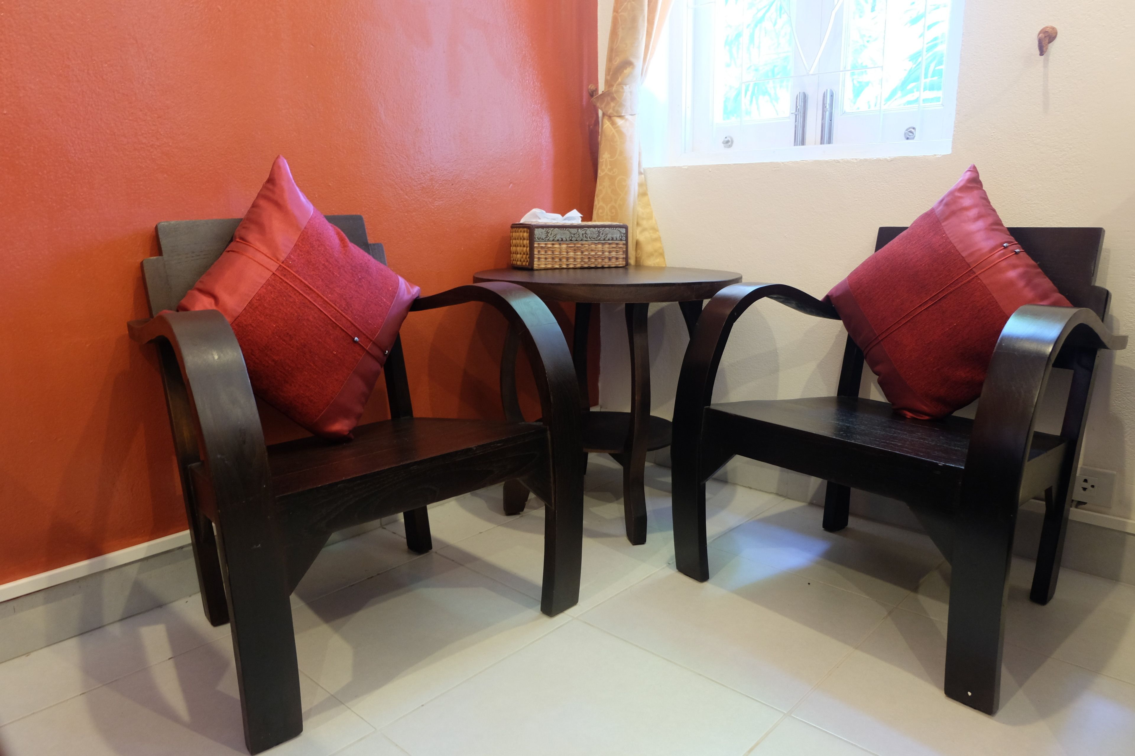 A room with two dark wooden chairs with red cushions, a small round table, and a tissue box.