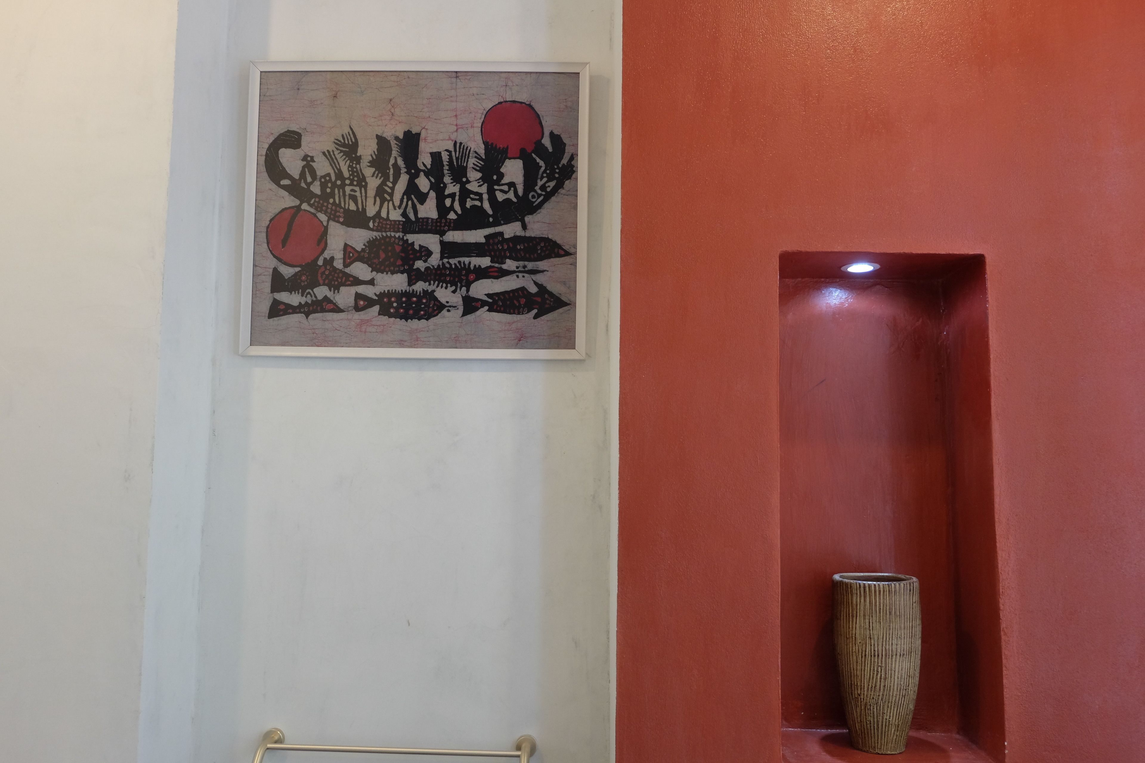 A framed artwork with abstract fish and a red circle on a white wall.