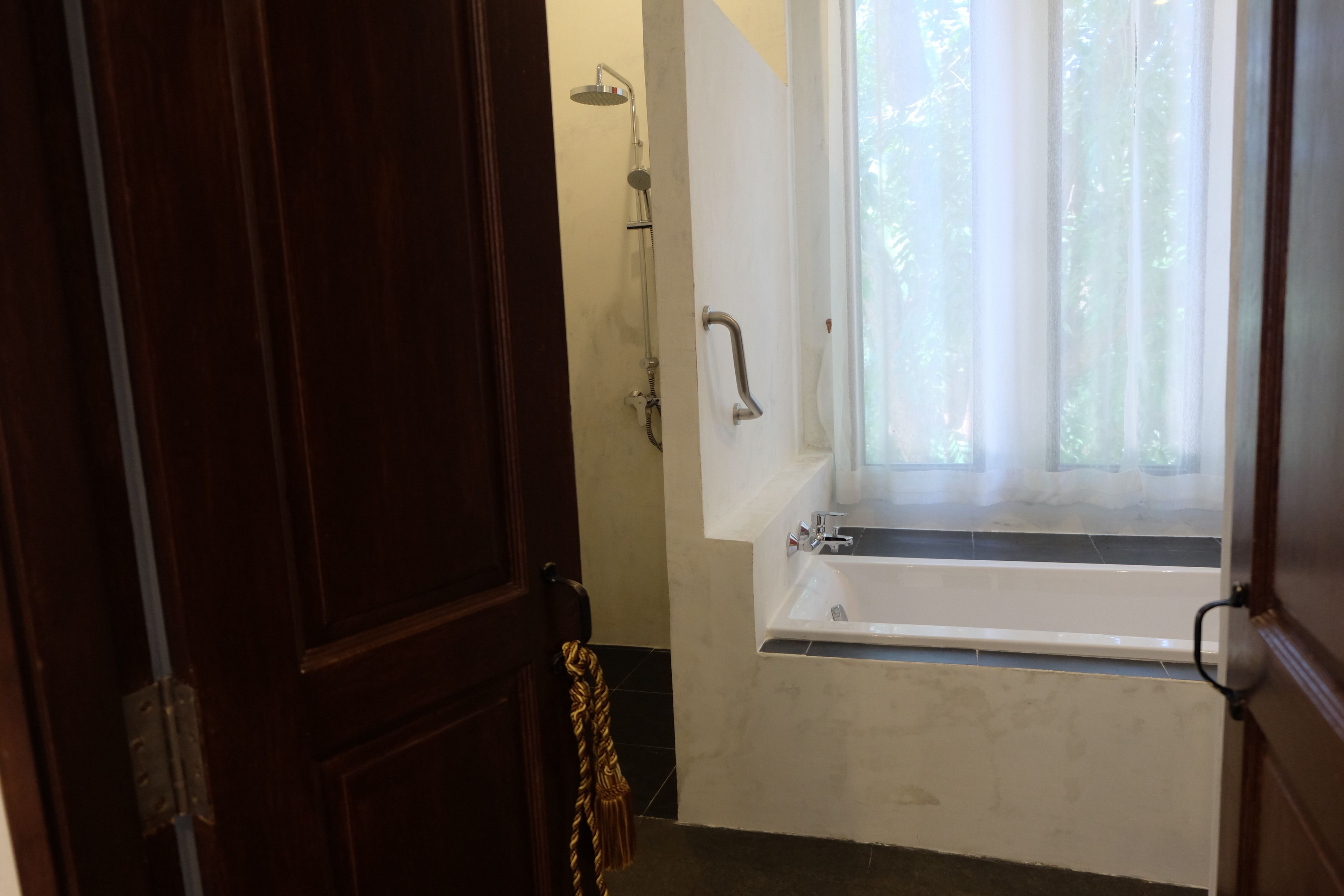 A bathroom with a bathtub, a shower, and a window with curtains.