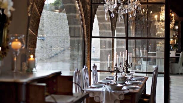 A dining area with a chandelier, a table set for four, and a view through large windows. - Hotel La Vella Farga (Lladurs)