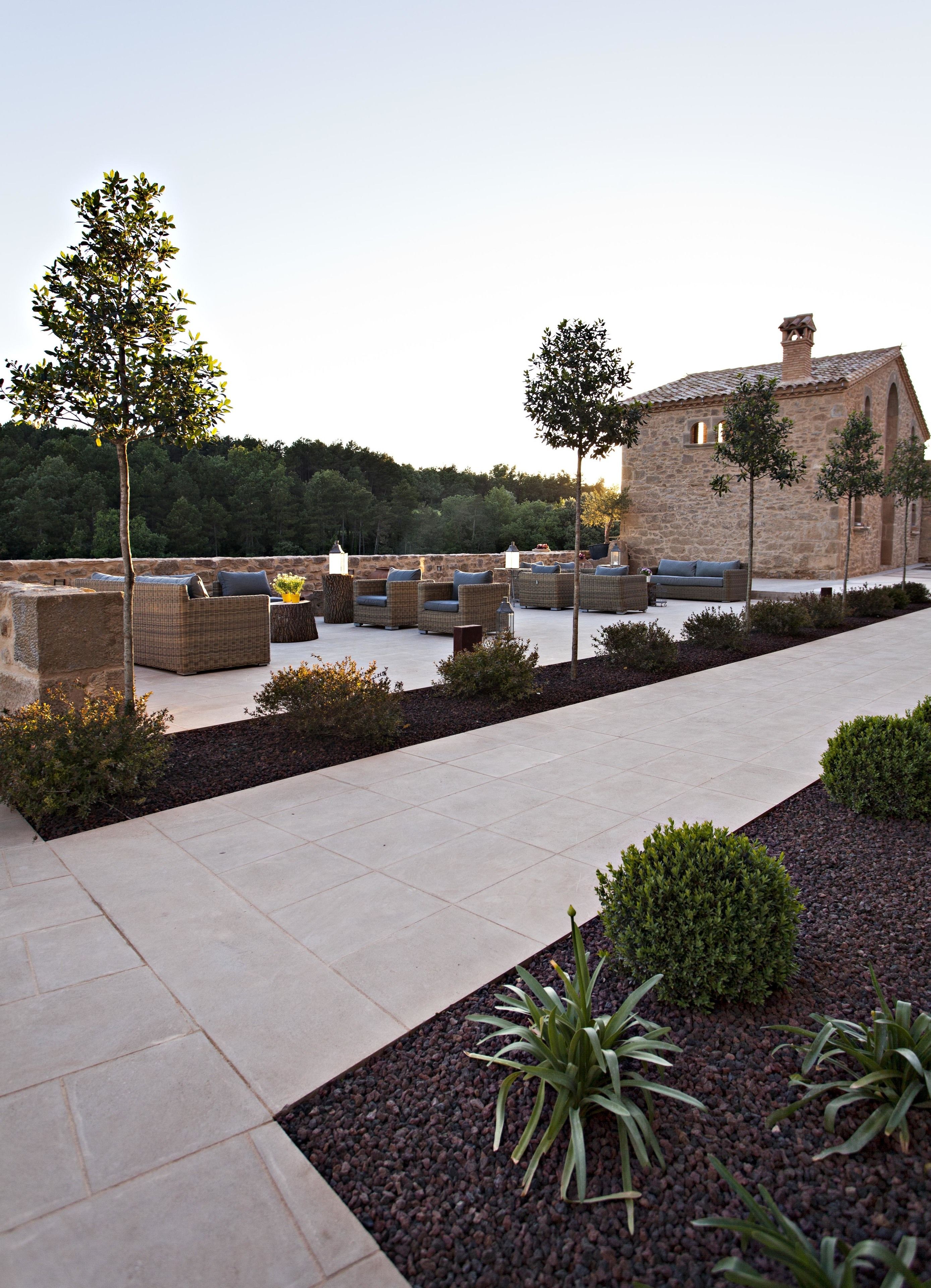 Terraço no telhado com móveis de vime, um edifício de pedra e um jardim paisagístico.