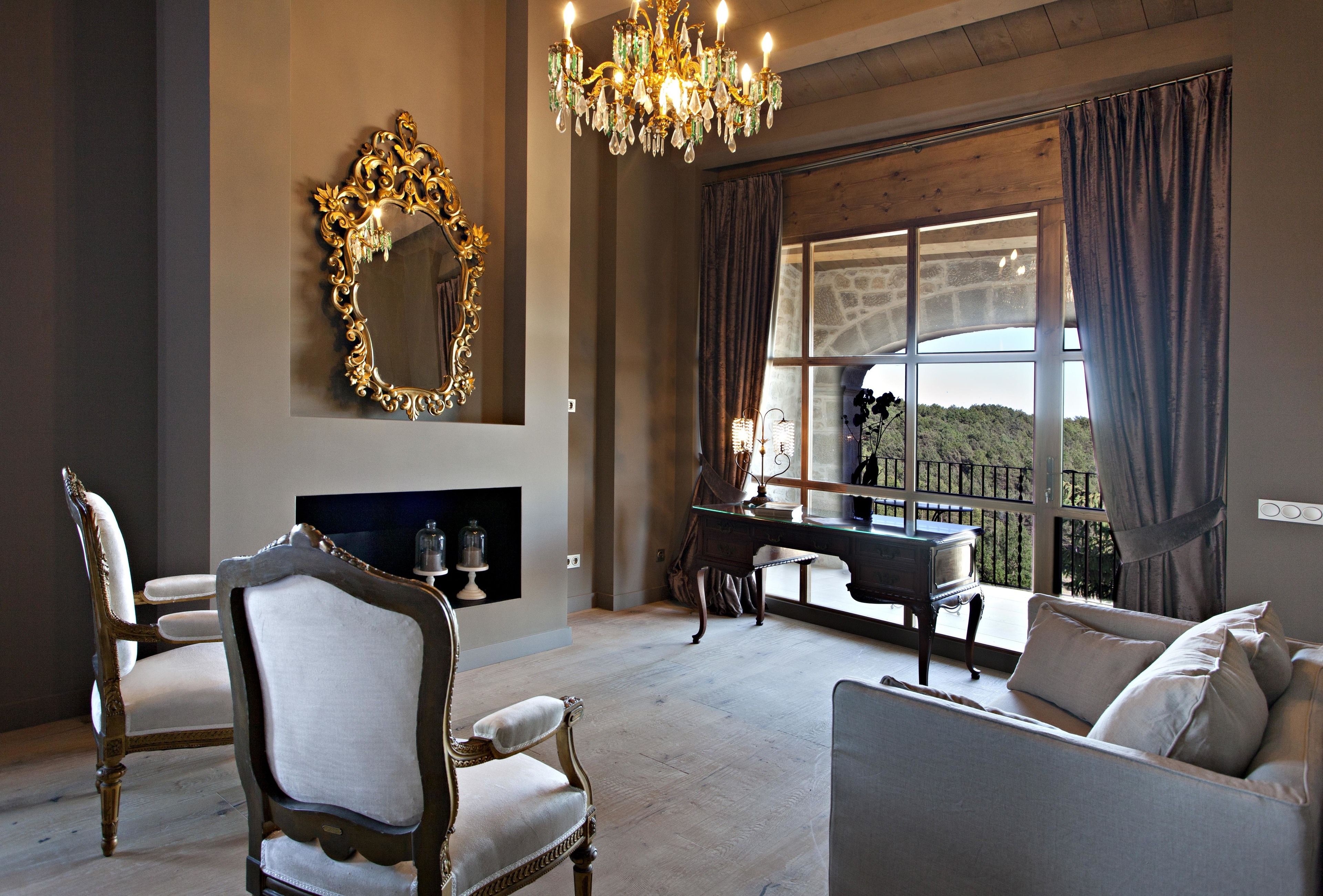 A living room with a large mirror, a chandelier, a fireplace, and a view of the outdoors.