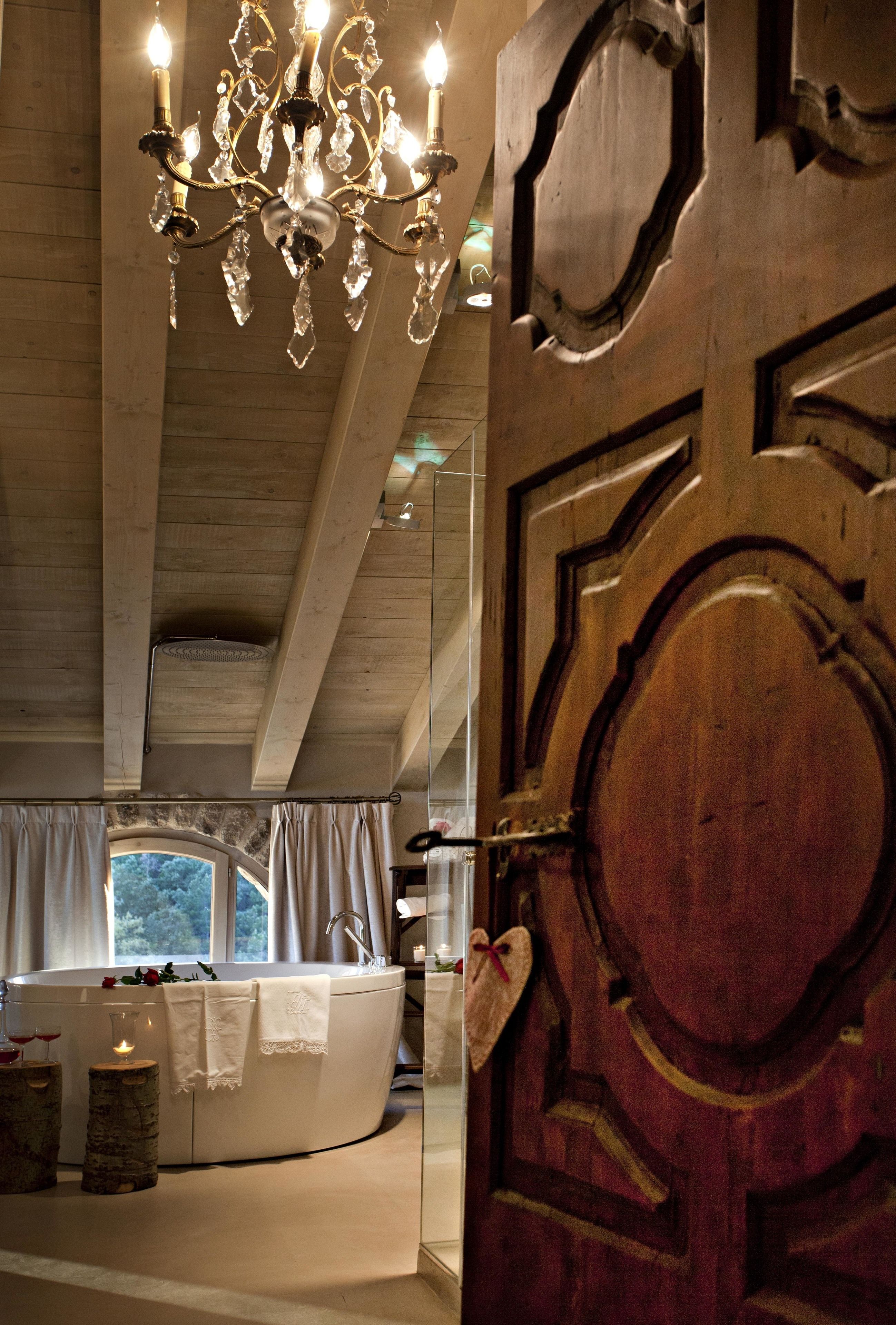 Ein luxuriöses Badezimmer mit freistehender Badewanne, einem Kronleuchter und einer großen Holztür.