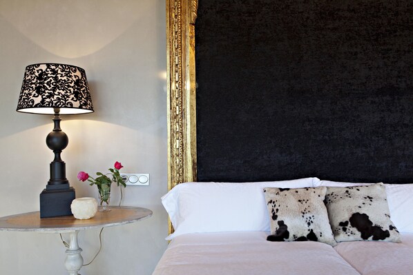 Un dormitorio con una cama, una mesita de noche con lámpara y un jarrón con flores.