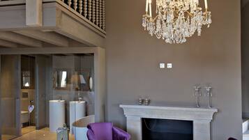 Un amplio salón con una imponente araña, dos sillones morados, chimenea y un baño con paredes de cristal.
