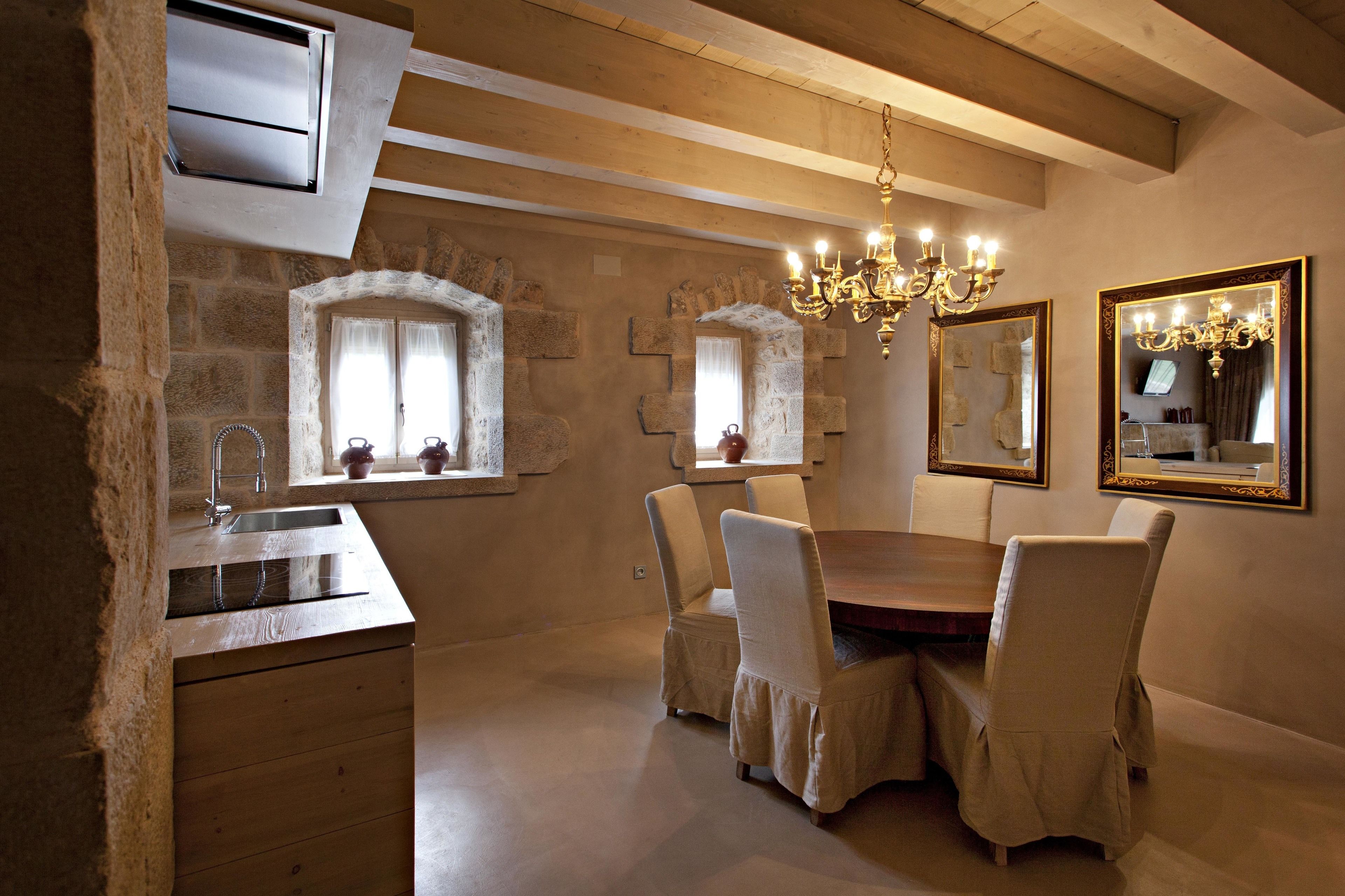 Un comedor con una mesa y sillas de madera, paredes de piedra y una araña.