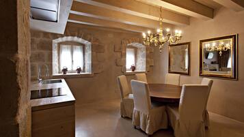 Un comedor con una mesa y sillas de madera, paredes de piedra y una araña.