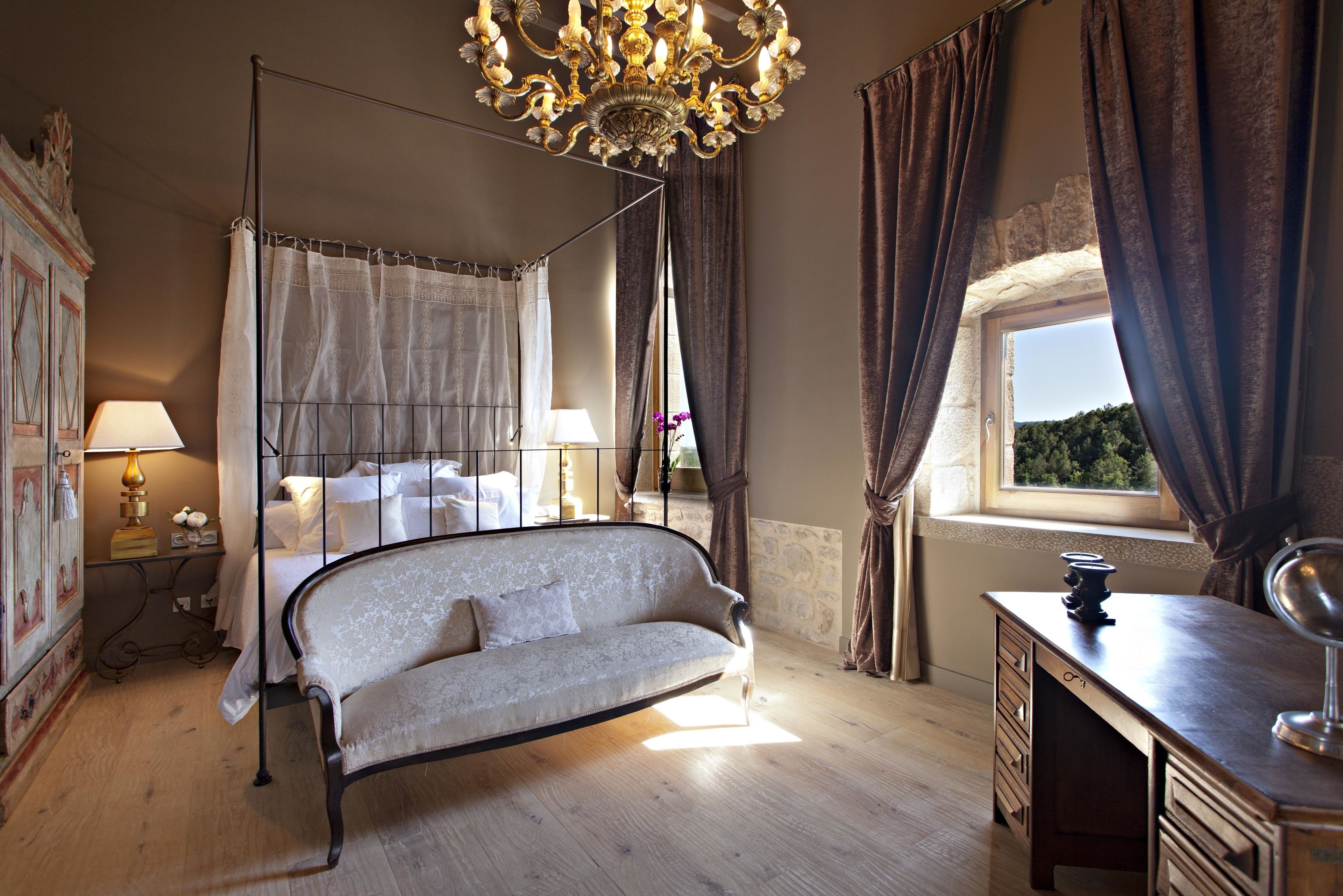 Un dormitorio con una cama con dosel, una chaise longue, un escritorio y un ventanal con cortinas.