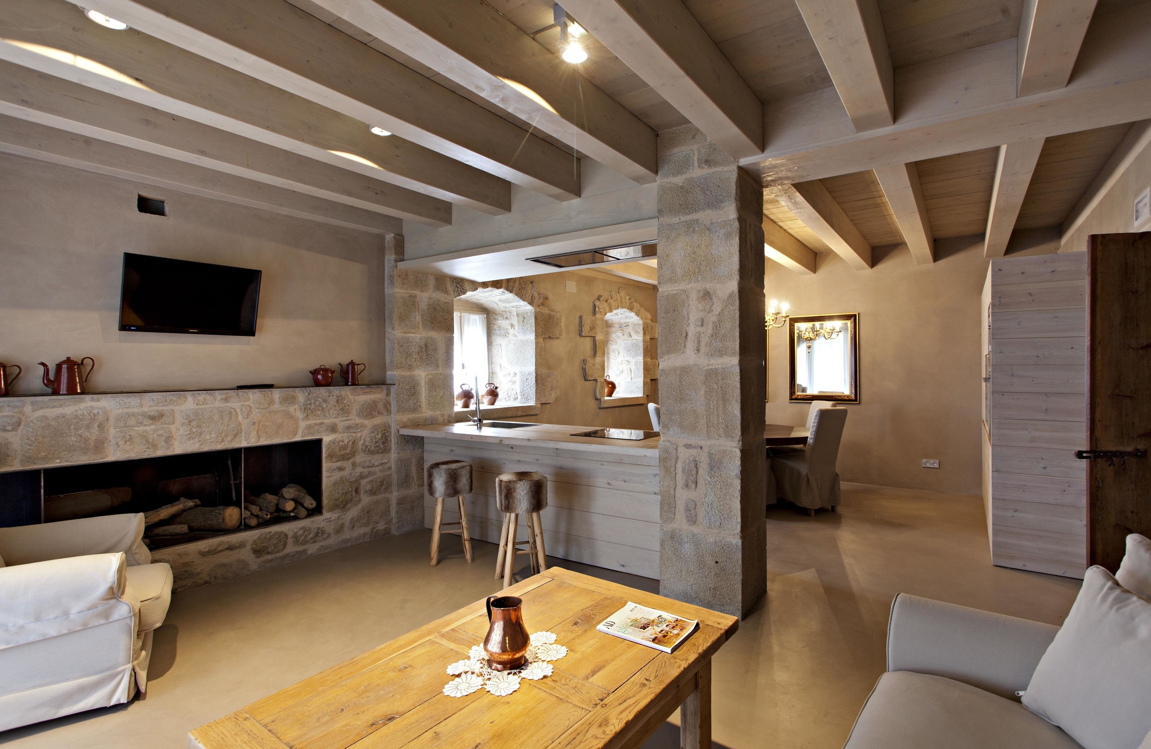 Un intérieur rustique avec des murs en pierre apparentes, une cheminée, une table en bois ornée d’un vase et un téléviseur fixé au mur.