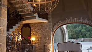 A spacious room with a stone staircase, a large chandelier, a cowhide rug, and a view through an arched window. - Hotel La Vella Farga (Lladurs)