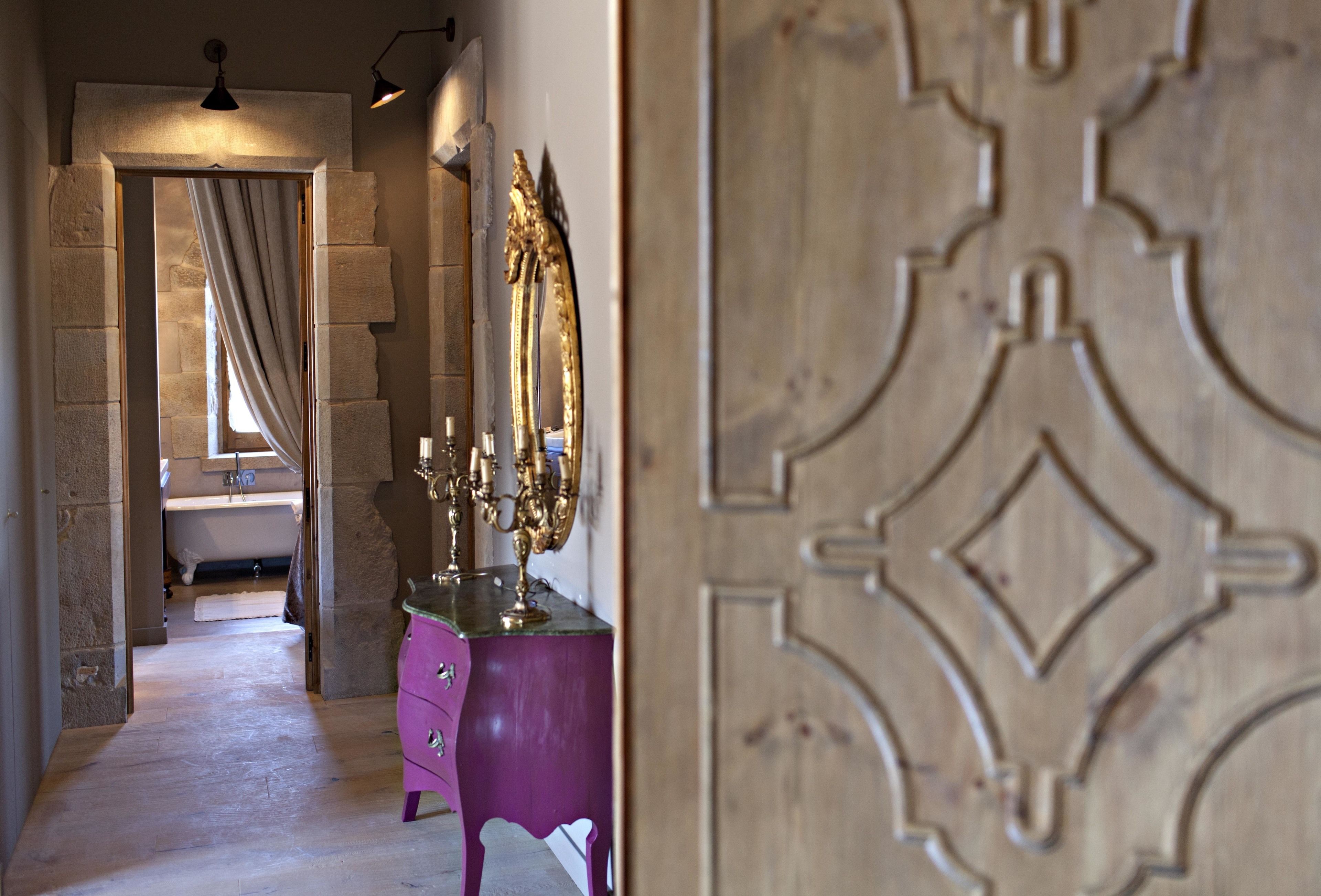 A narrow hallway leading to a bathroom with a bathtub, a vanity with a mirror, and a door with an ornate design.