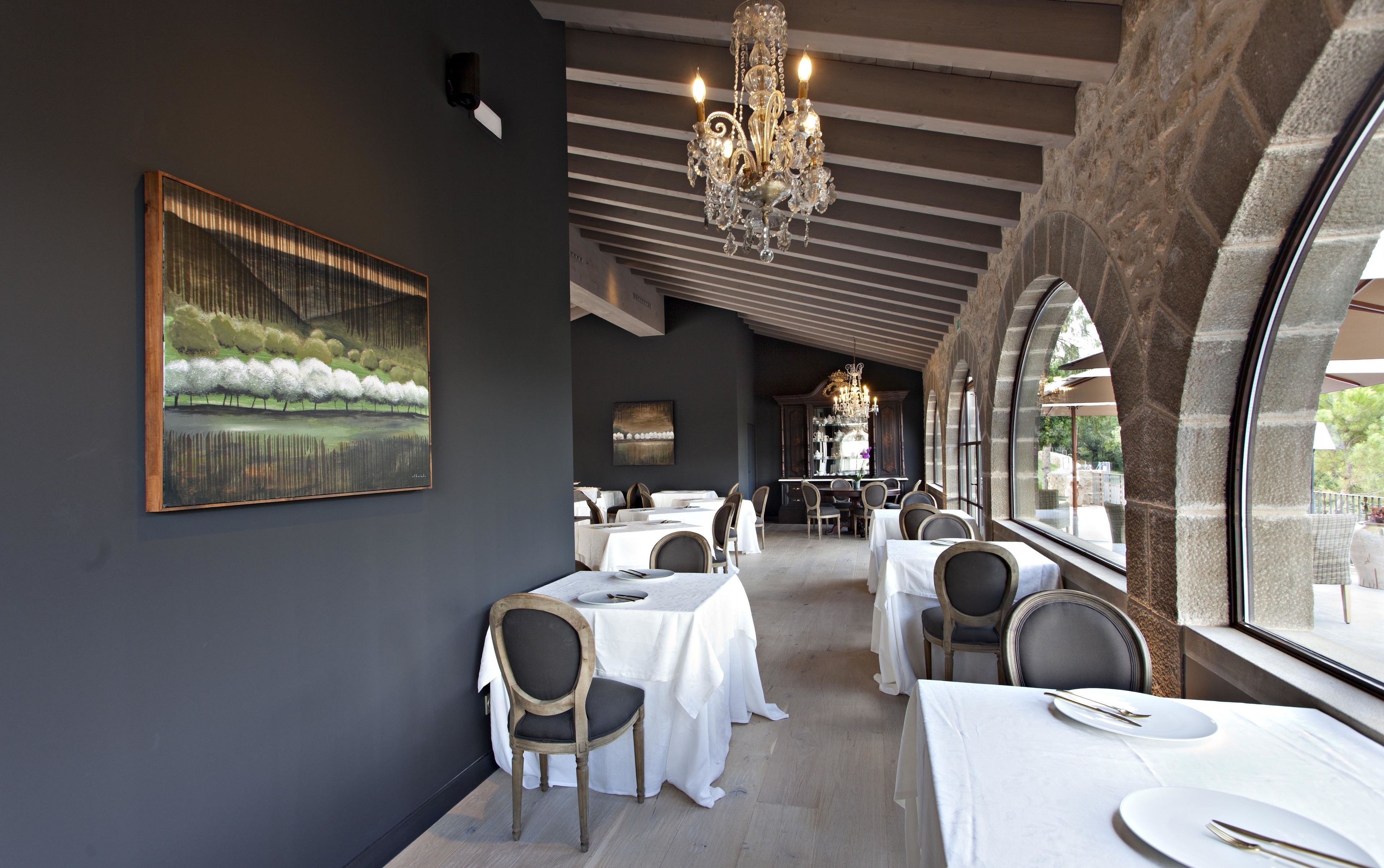 A restaurant with a modern interior, featuring a chandelier, white tablecloths, and a large painting on the wall.
