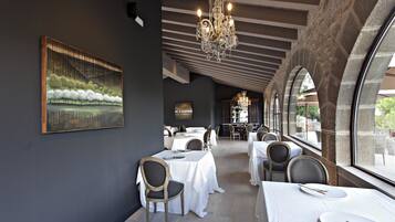 A restaurant with a modern interior, featuring a chandelier, white tablecloths, and a large painting on the wall.