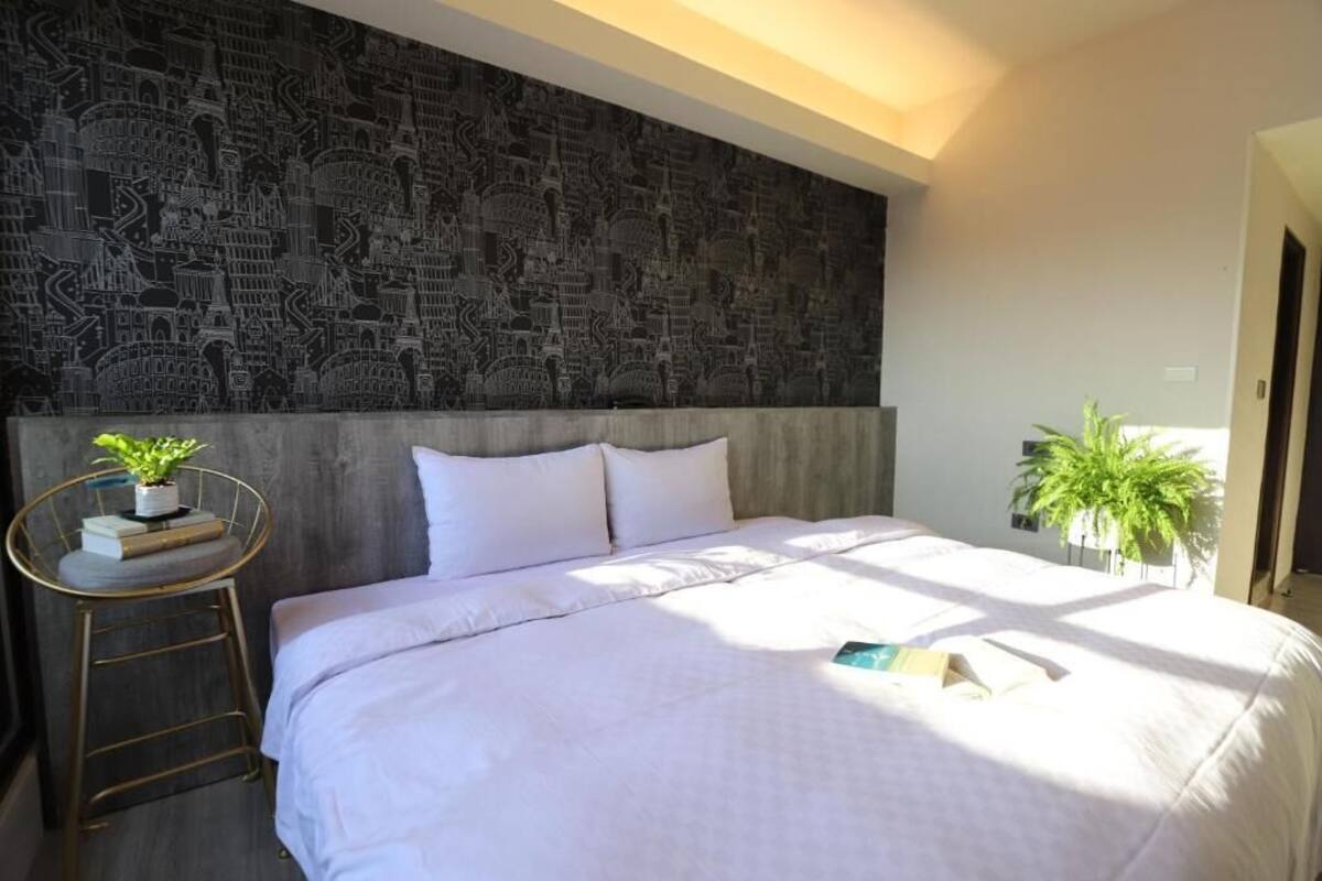 Quarto com cama grande, cabeceira com design de paisagem urbana, mesinha de cabeceira com planta e escada.
