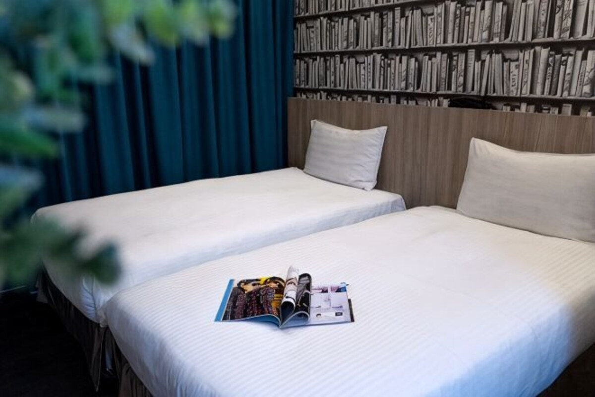 Een hotelkamer met twee bedden, een boekenplank en een tijdschrift op het bed.