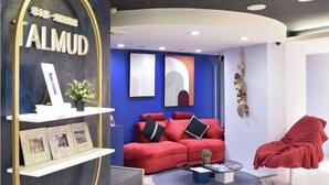 Un saló modern amb un sofà vermell, una taula de centre i un butac armchair vermell. Hi ha una estant blanca amb quadres emmarcats i una planta.