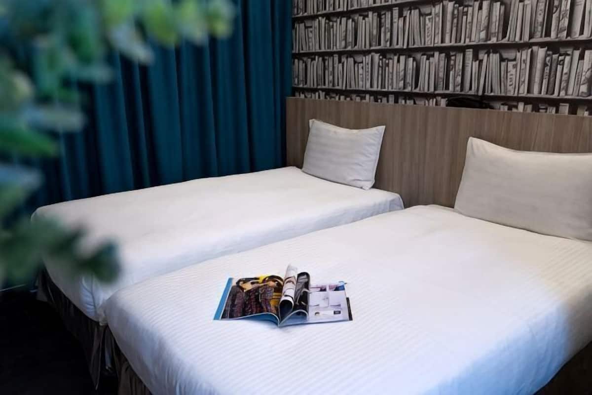 Quarto de hotel com duas camas, uma estante de livros e uma revista sobre a cama.