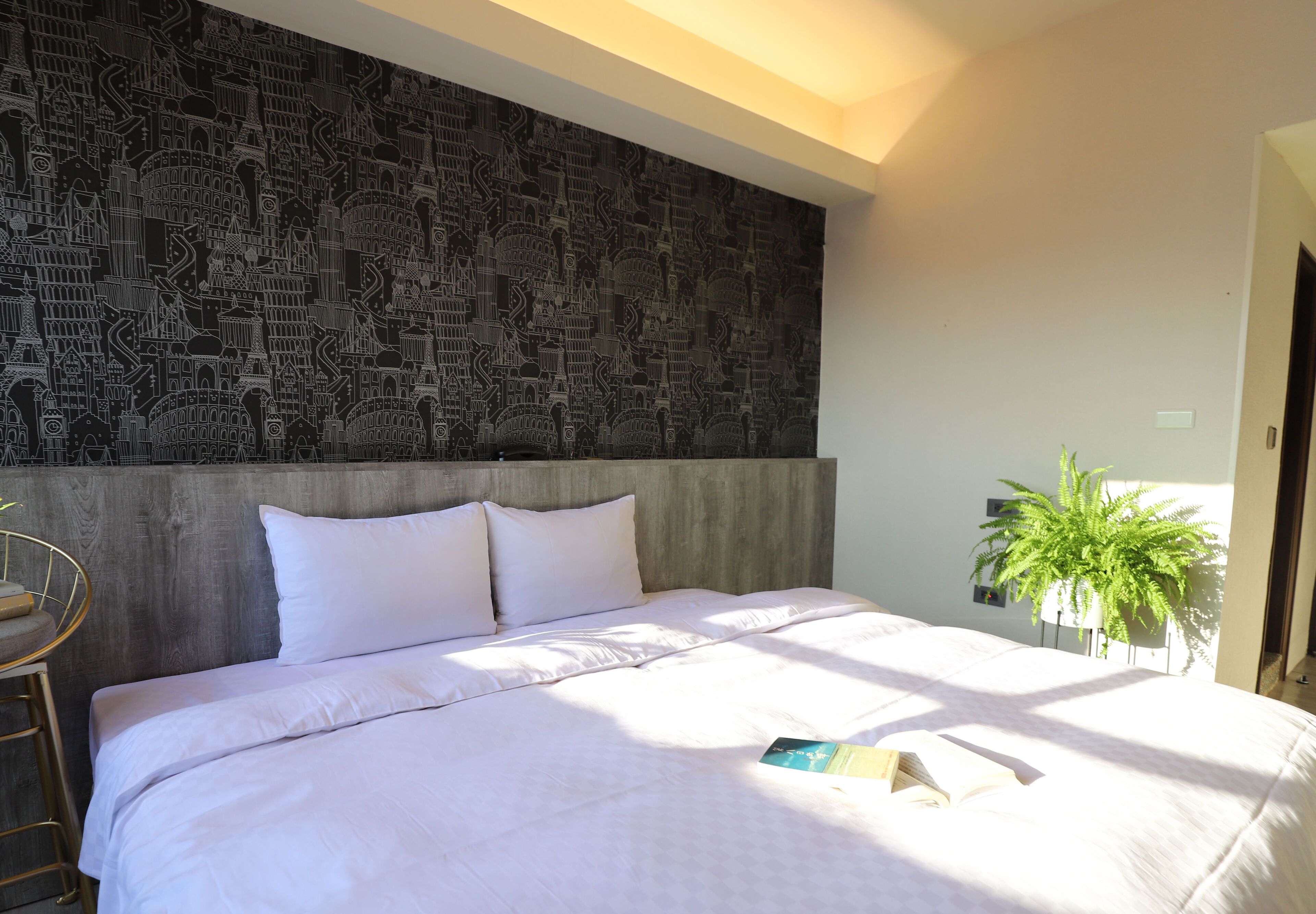 Une chambre avec un grand lit, du linge de lit blanc, un mur à motifs et une plante en pot.
