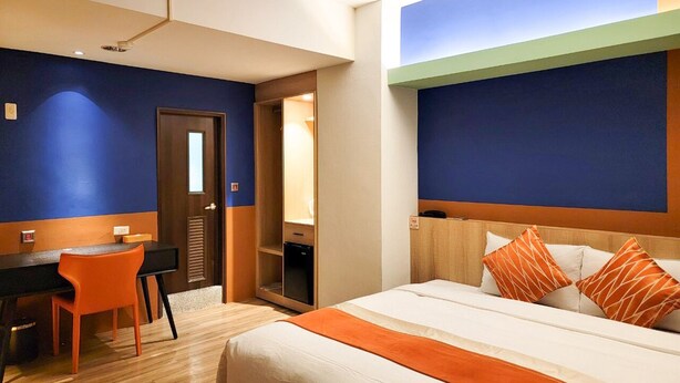 Habitació d'hotel amb un llit, una taula i una cadira. Hi ha una porta que dona a una altra habitació.