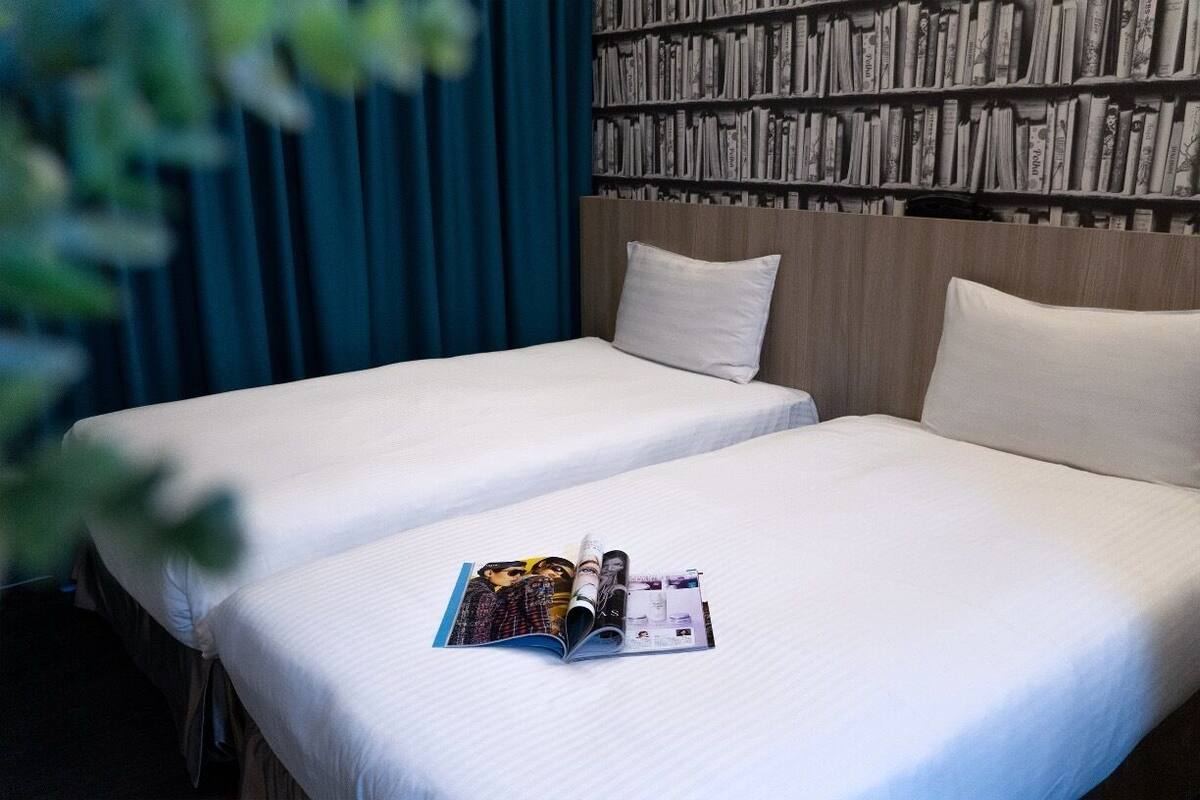 Quarto de hotel com duas camas, uma estante de livros e uma revista sobre a cama.