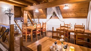 Un espace de salle à manger en bois, doté de hauts plafonds et de poutres apparentes, comprenant un escalier et offrant une vue sur une fenêtre.