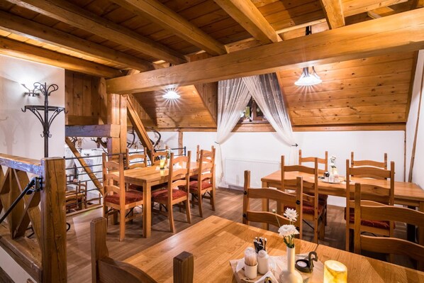 A wooden dining area with high ceilings and exposed beams, featuring a staircase and a view of a window.