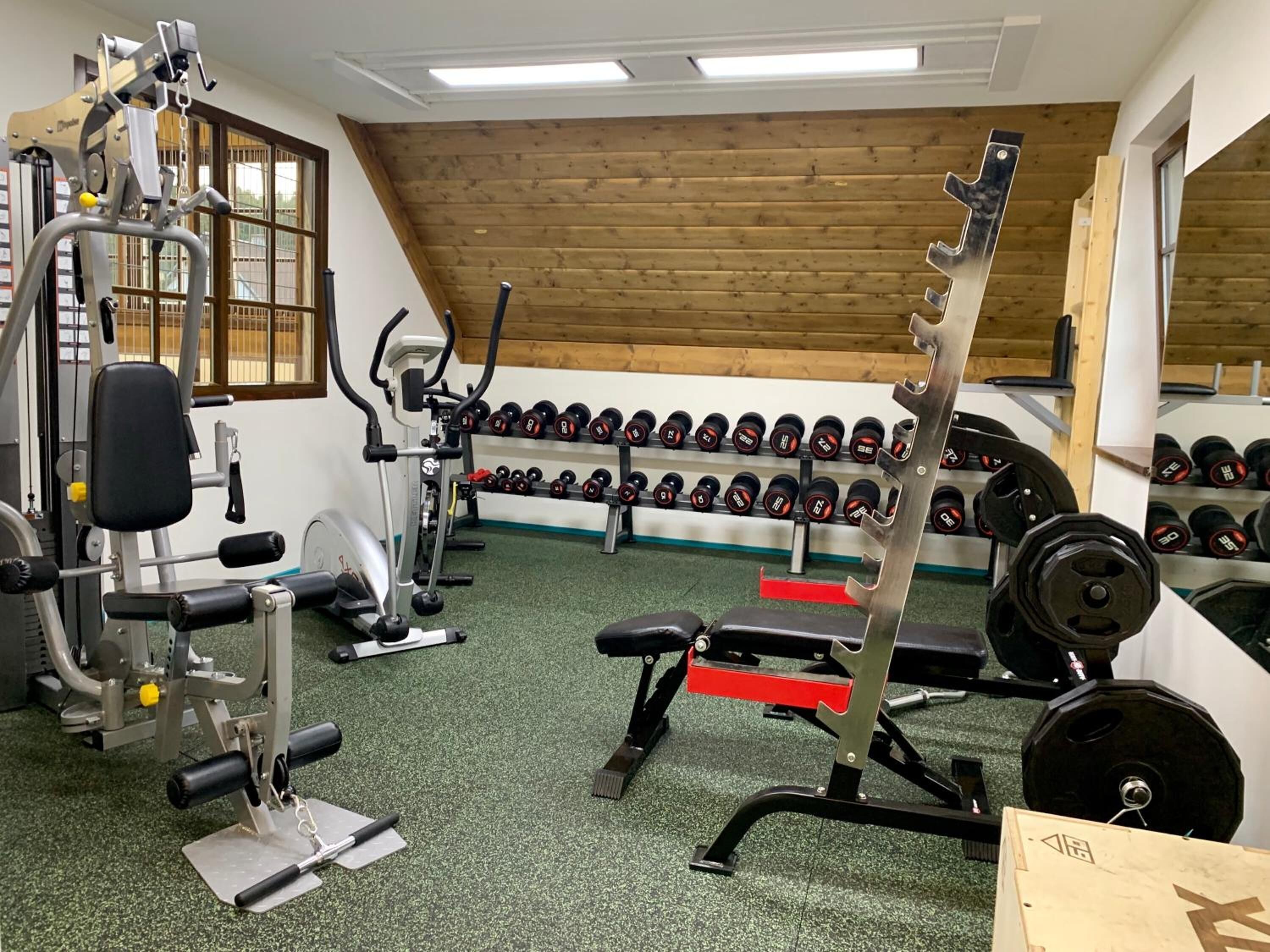 Et fitnessrum med forskellig træningsudstyr, herunder håndvægte, en bænk og vægttræningsmaskiner.