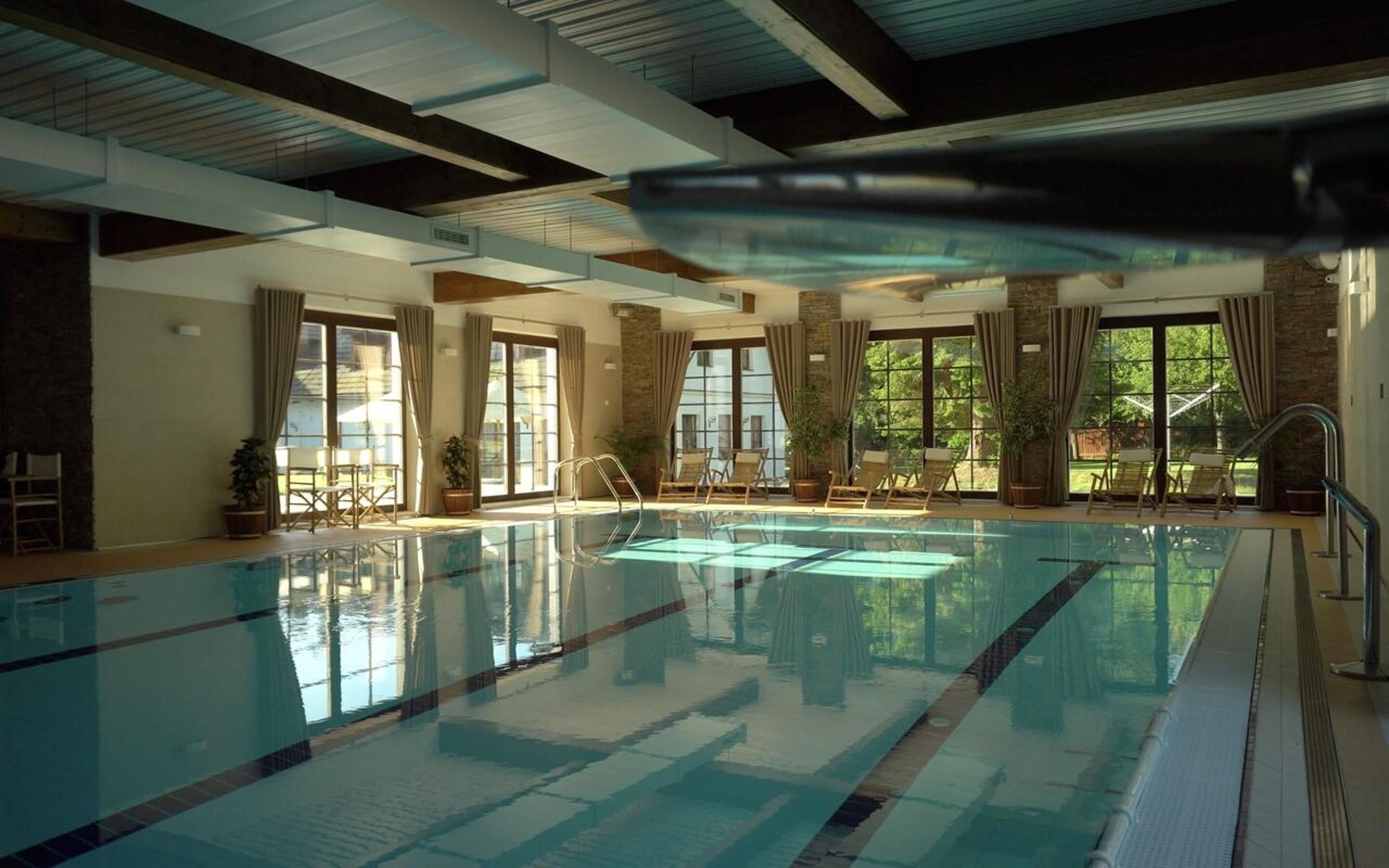 Piscina interna com água cristalina, rodeada por janelas e plantas em vasos.