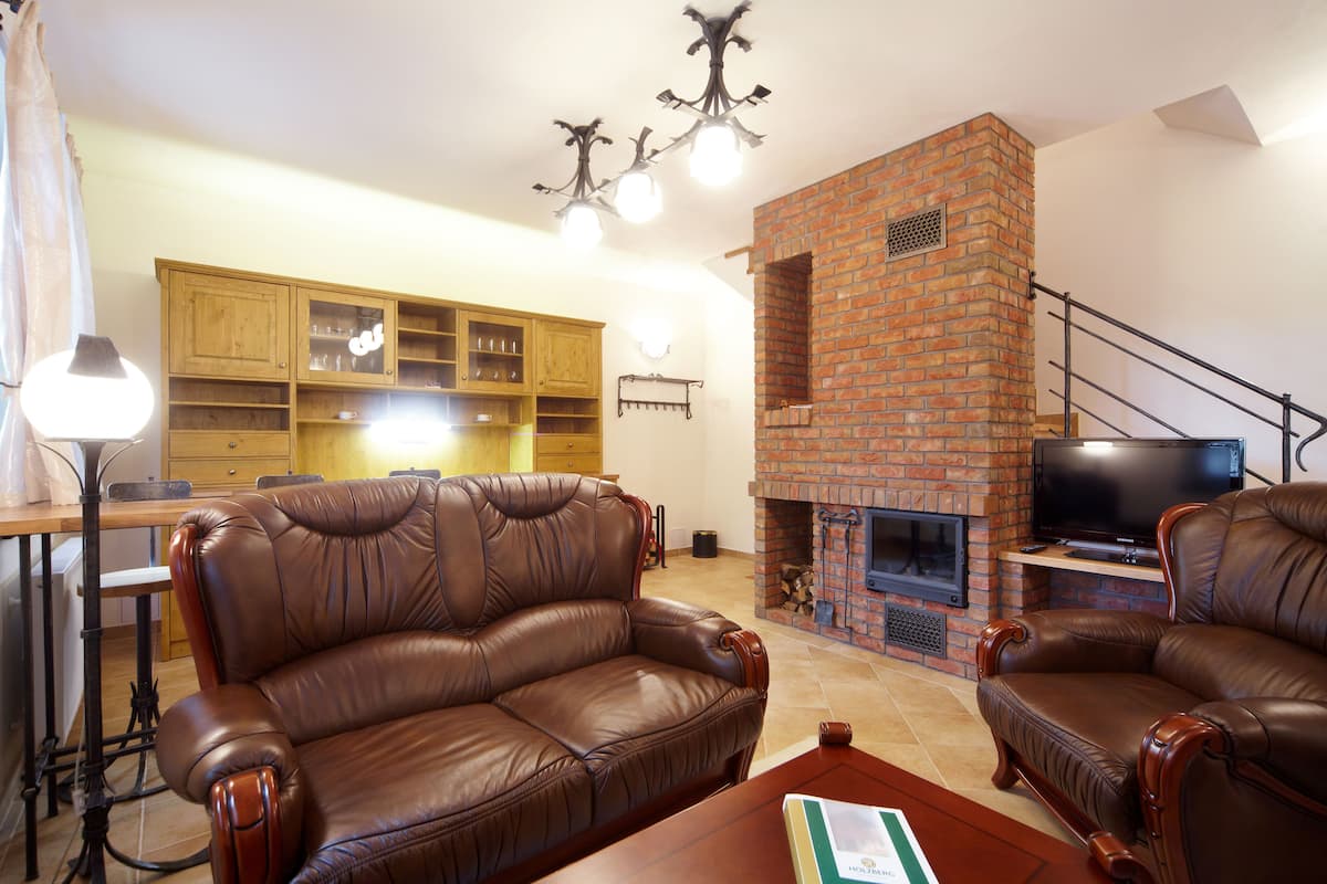 Una sala de estar con sofás de cuero, una chimenea de ladrillo, armarios de madera y un televisor.