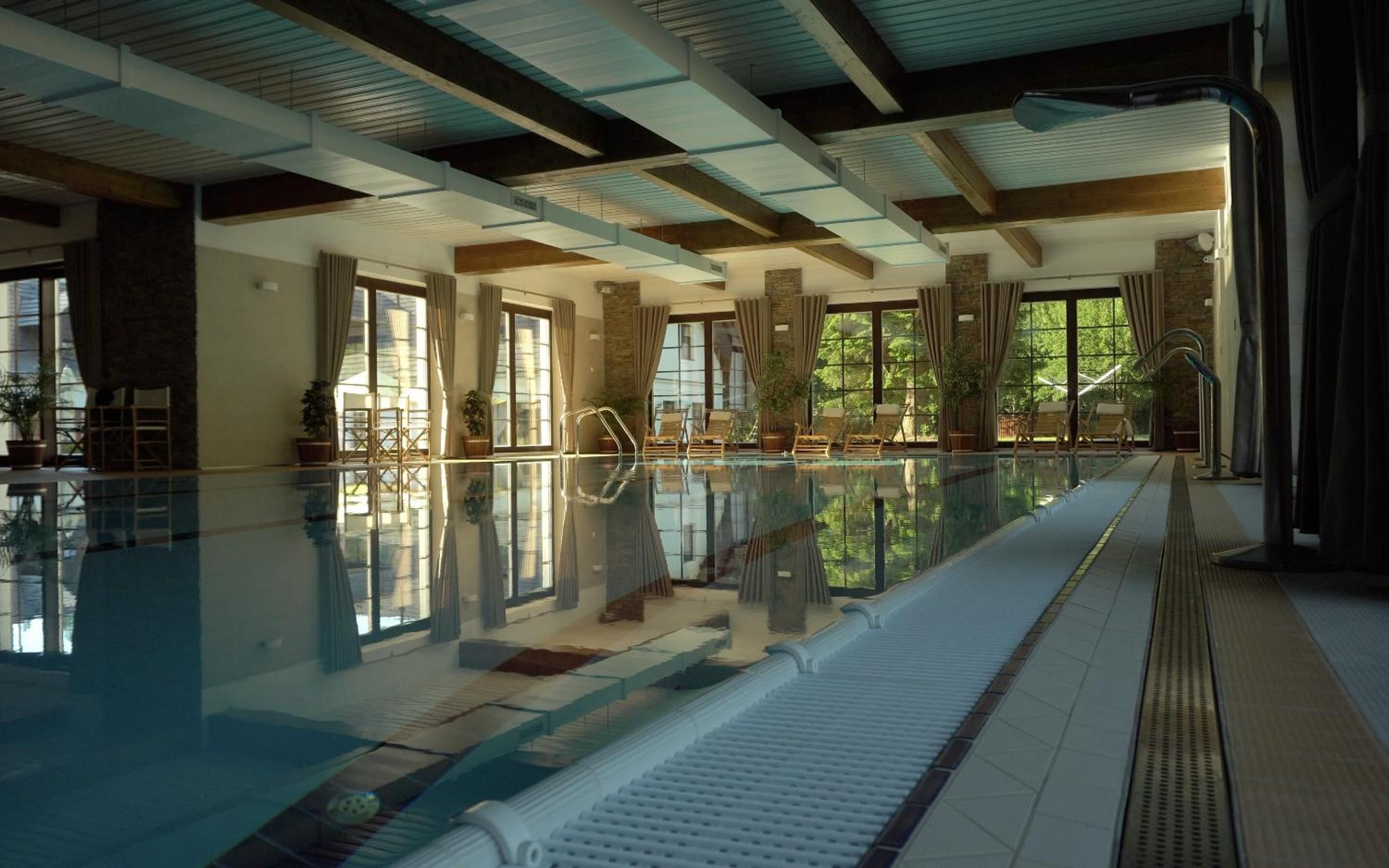 A large indoor swimming pool with clear water, surrounded by lounge chairs and potted plants.