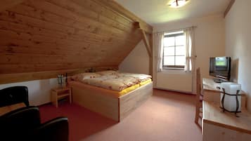 A bedroom with a sloped ceiling, wooden bed, desk, chair, and a television.