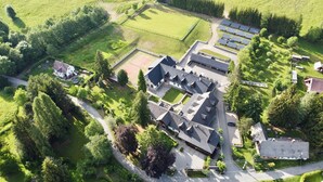 Vue aérienne d’un quartier résidentiel avec une grande maison, des panneaux solaires et de la végétation luxuriante tout autour.