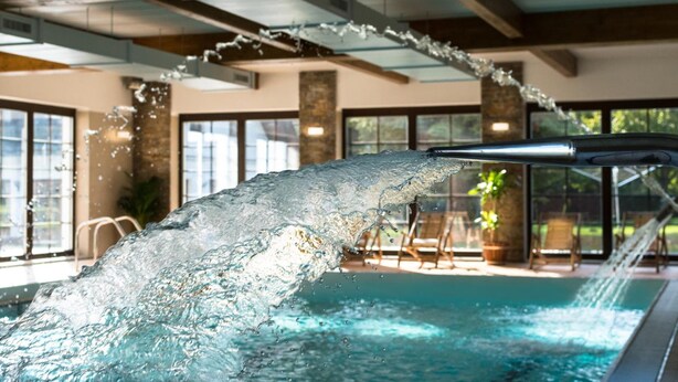Une piscine agrémentée d’un élément décoratif aquatique, un espace de détente intérieur et de grandes fenêtres.