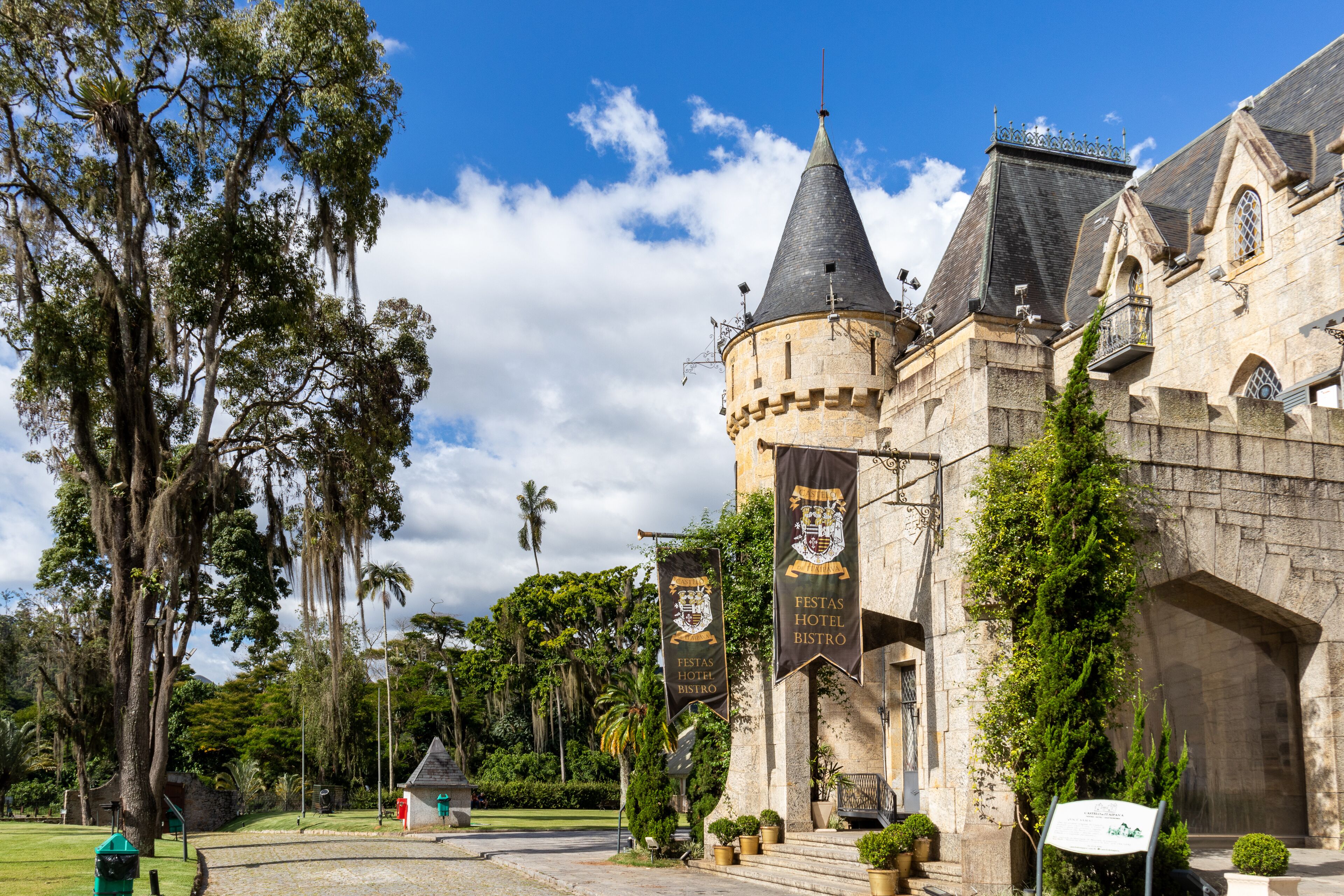 Un edificio histórico con una torre destacada, con banderines del hotel y el bistro, y abundante vegetación que rodea la propiedad.