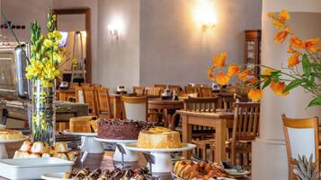 A buffet with various dishes, including cakes and fruits, in a dining area with wooden chairs and tables.