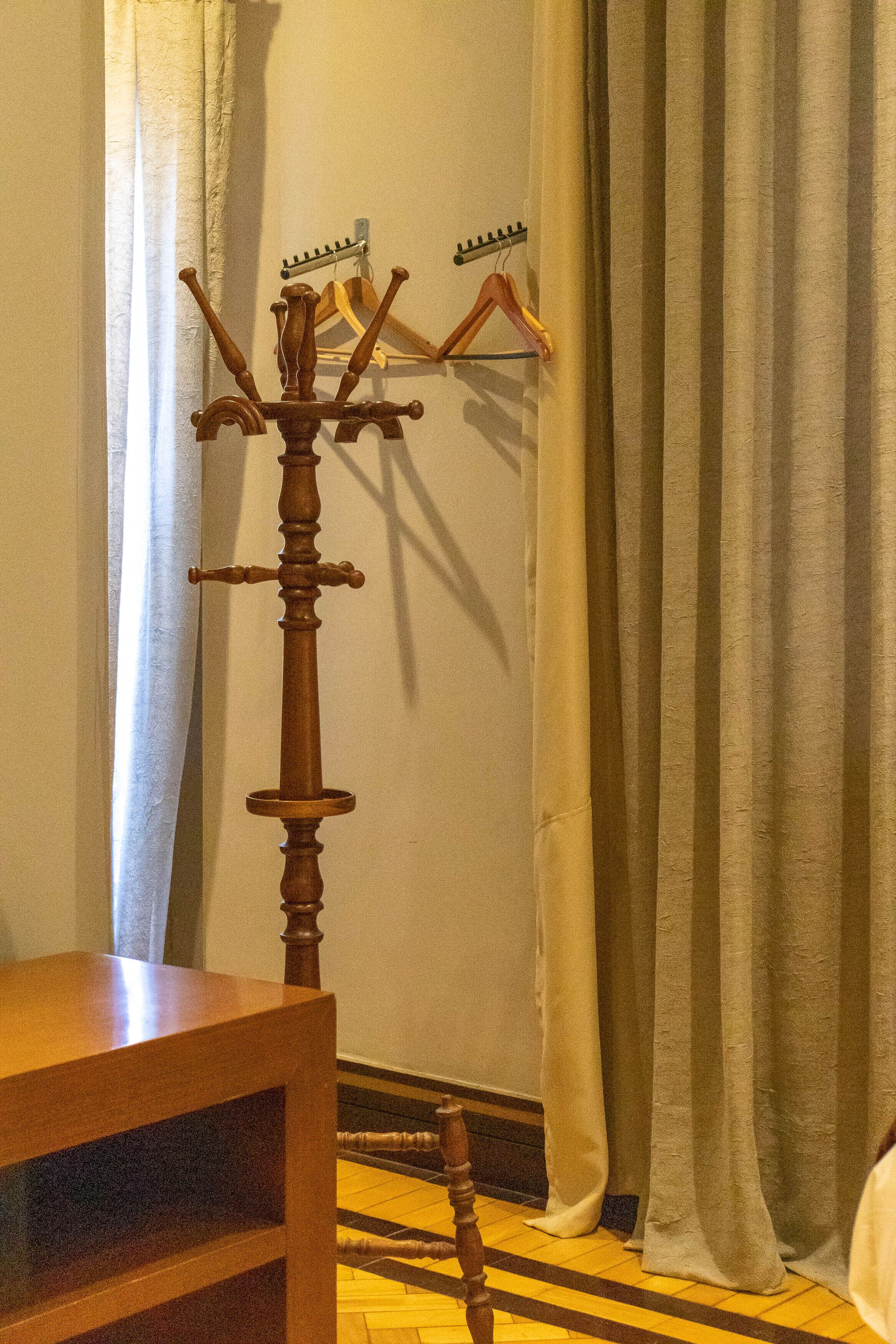 A wooden coat rack with multiple hooks and a small table in front of a curtain.