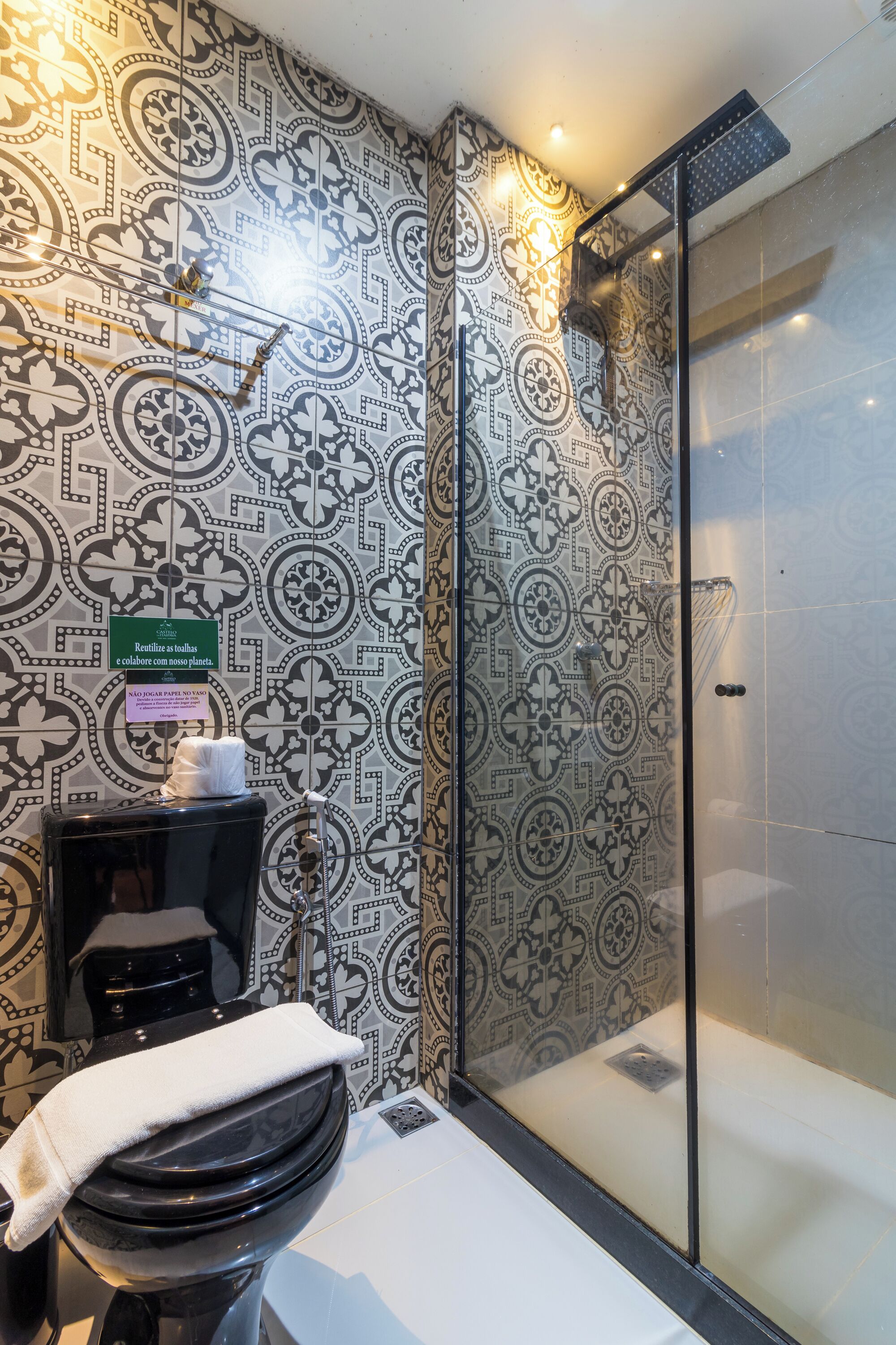 Ein Badezimmer mit gemusterten Fliesen, einer Duschkabine aus Glas und einem WC mit Handtuch.