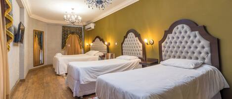 A hotel room with three beds, a chandelier, and a wooden floor.