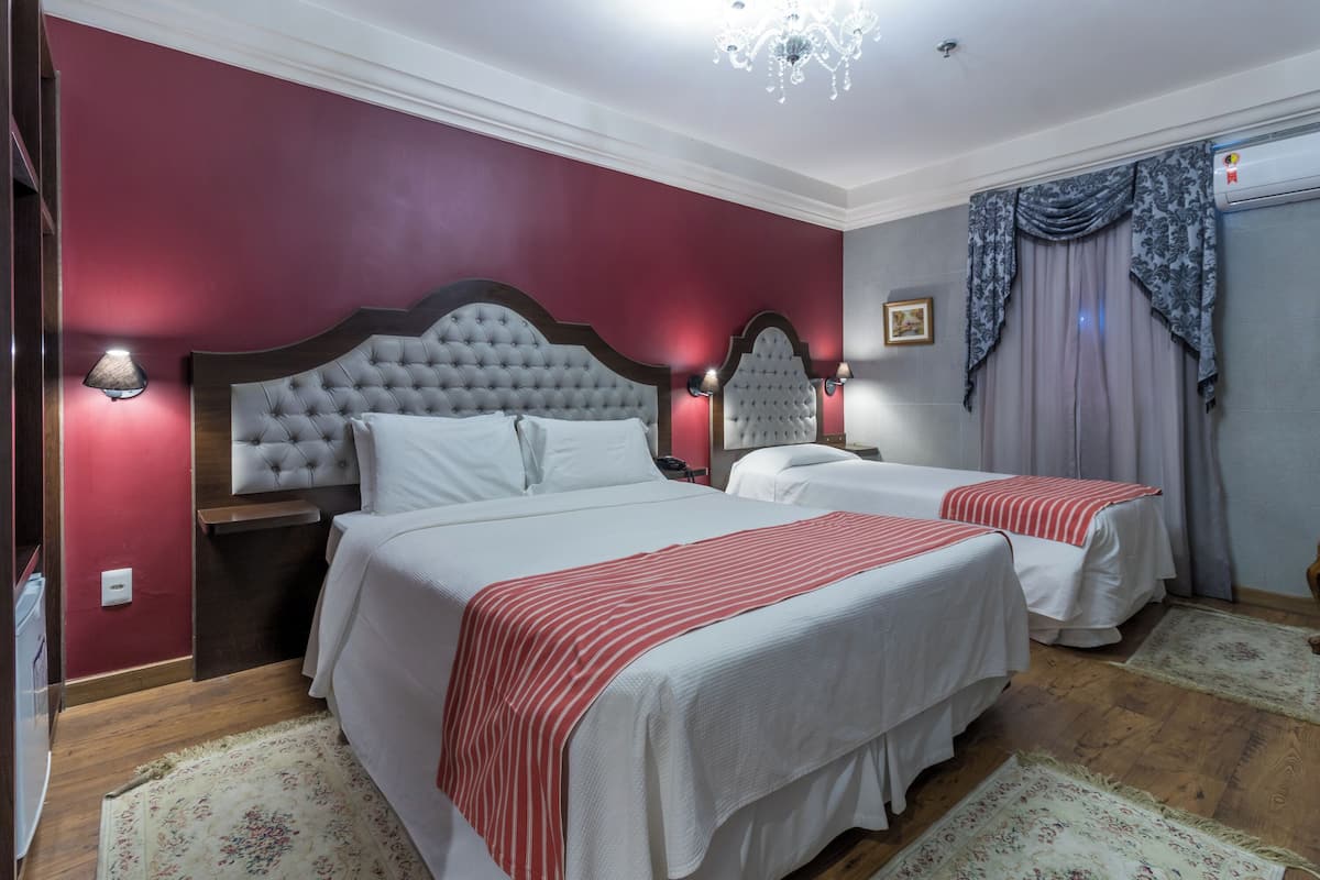 Ett hotellrum med två sängar, en kristallkrona och en röd accentvägg.