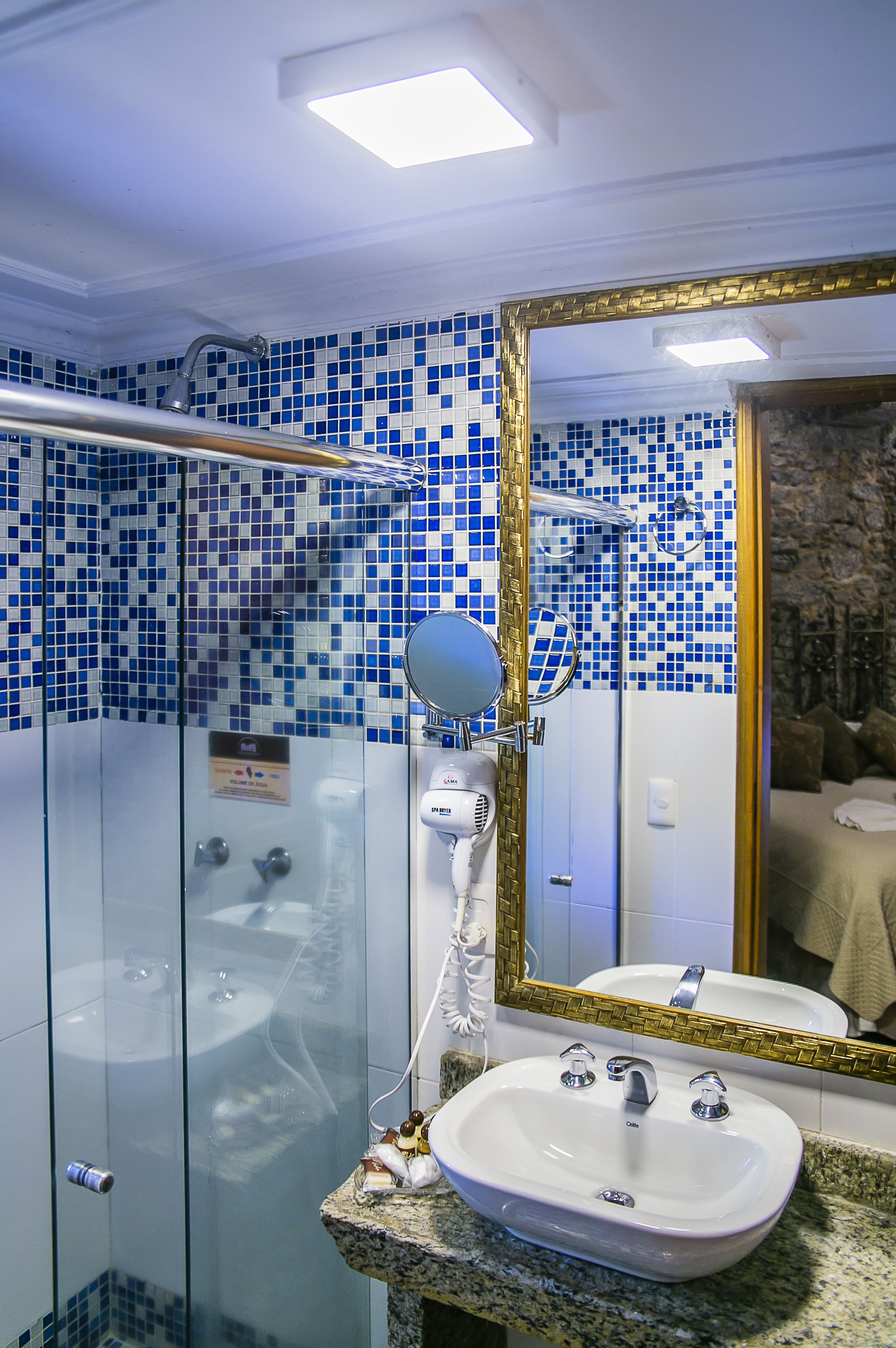 A bathroom with a white sink, a mirror with a gold frame, and blue mosaic tiles on the walls.