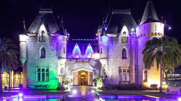 Un edificio al estilo de castillo con una entrada central, dos torres y un foso que lo rodea.