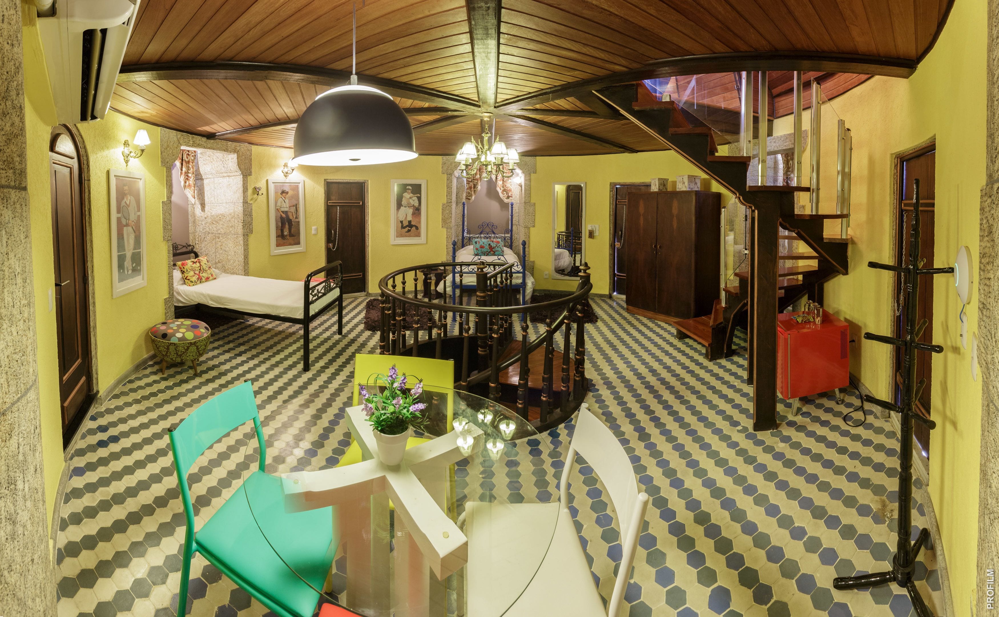 Un coin repas avec une table ronde, des chaises et un lustre. On y trouve un escalier avec une rampe en bois et une boîte rouge sur le côté.