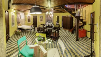 Un coin repas avec une table ronde, des chaises et un lustre. On y trouve un escalier avec une rampe en bois et une boîte rouge sur le côté.